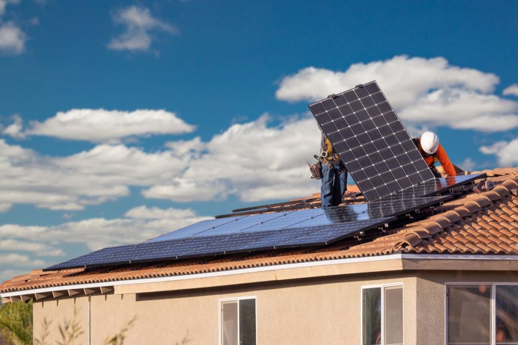 A man installs solar panels on a roof, demonstrating renewable energy efforts in a residential setting.